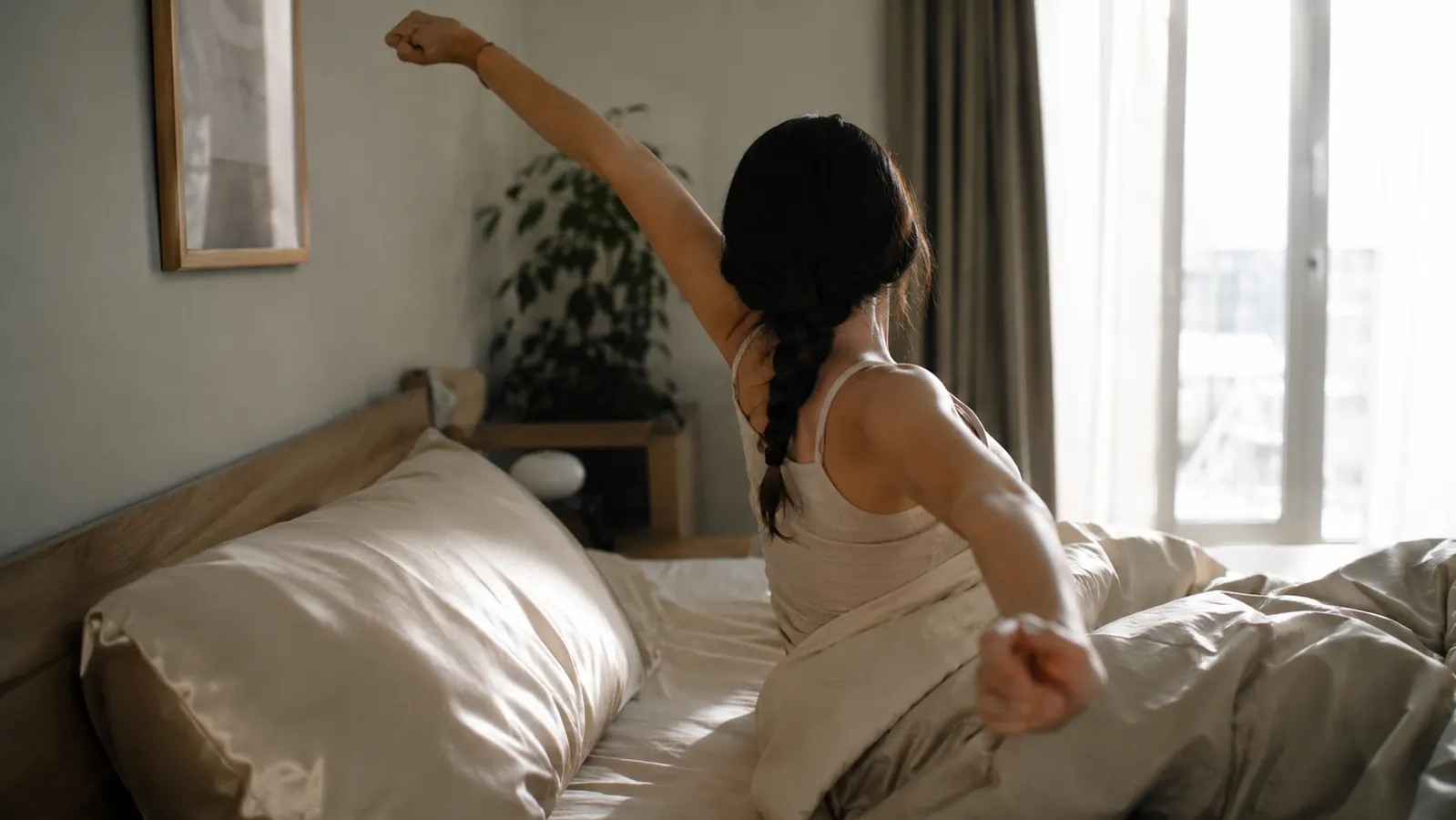A woman waking up with a braid still intact, sitting up in bed next to a silk pillowcase