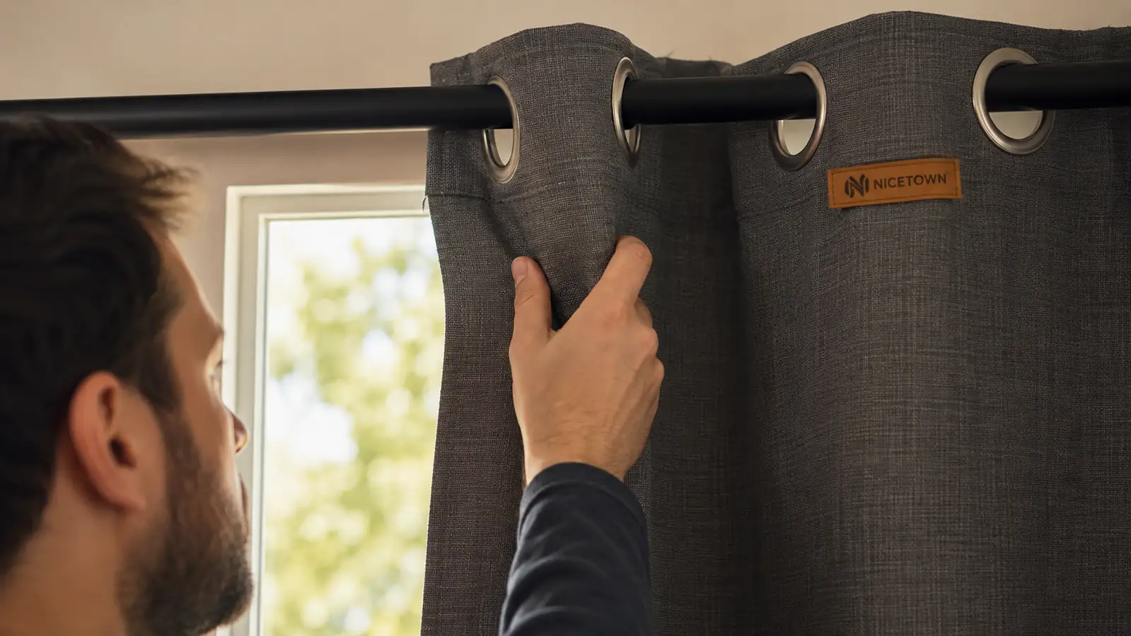 Hand pulling a grey grommet blackout curtain closed along the rod, using the actual NICETOWN panel as reference