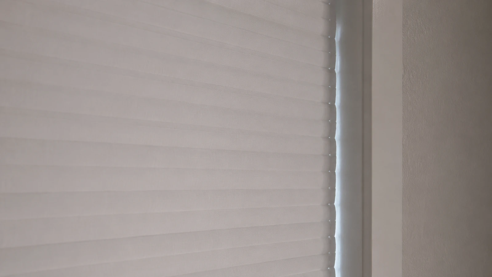 Close-up of a thin line of light leaking along the edge of a closed cellular blackout blind against a window frame