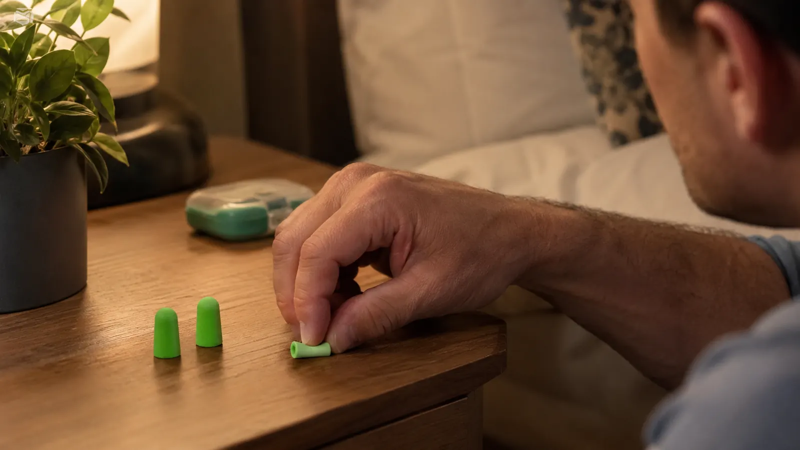 A hand rolling a green foam Flents ear plug between two fingers before inserting it