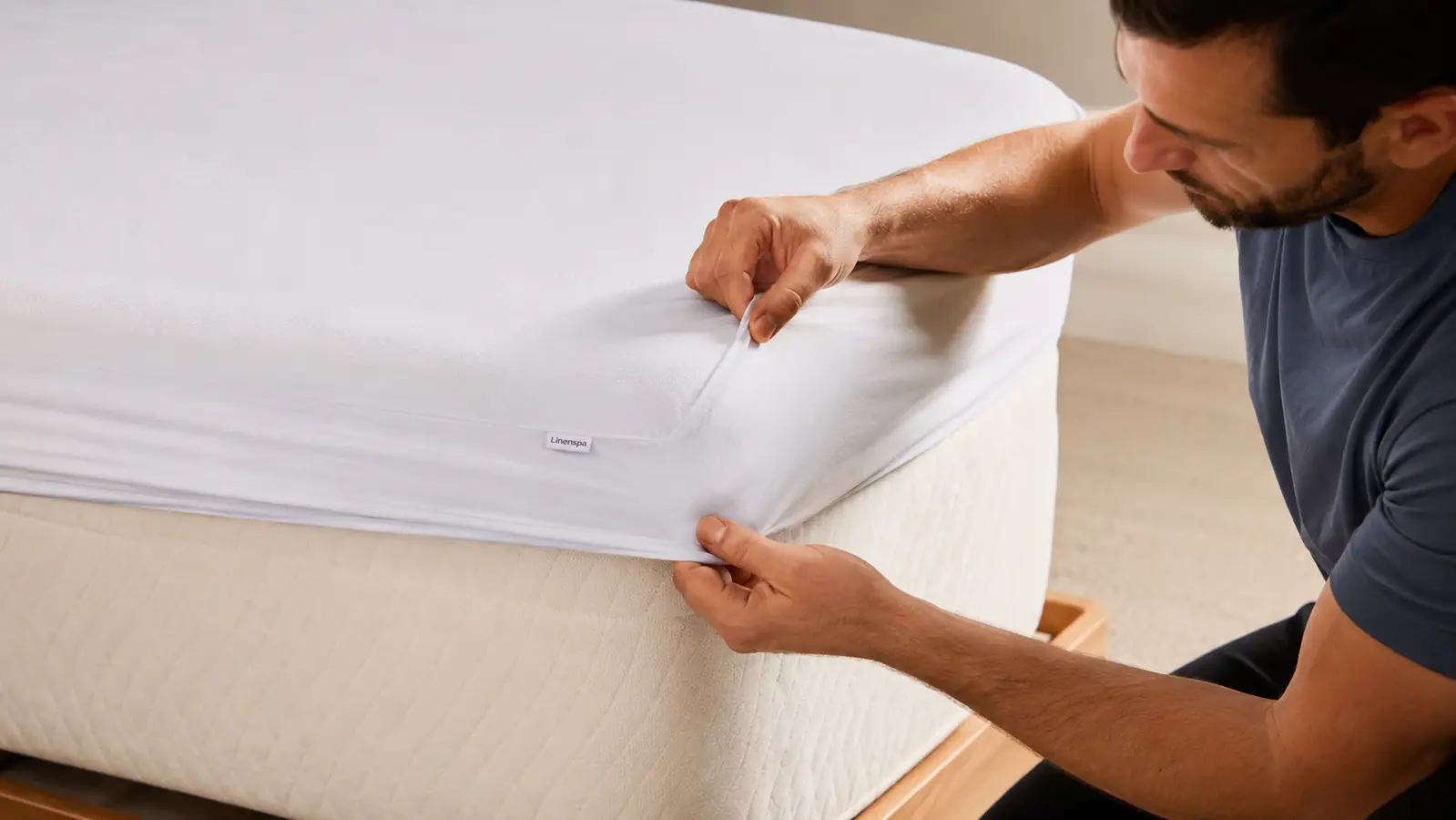 Hands pulling the fitted corner of a white mattress protector snugly over a mattress corner