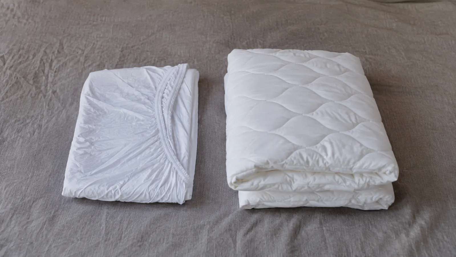 A thin waterproof mattress protector laid flat beside a thicker quilted mattress pad for comparison