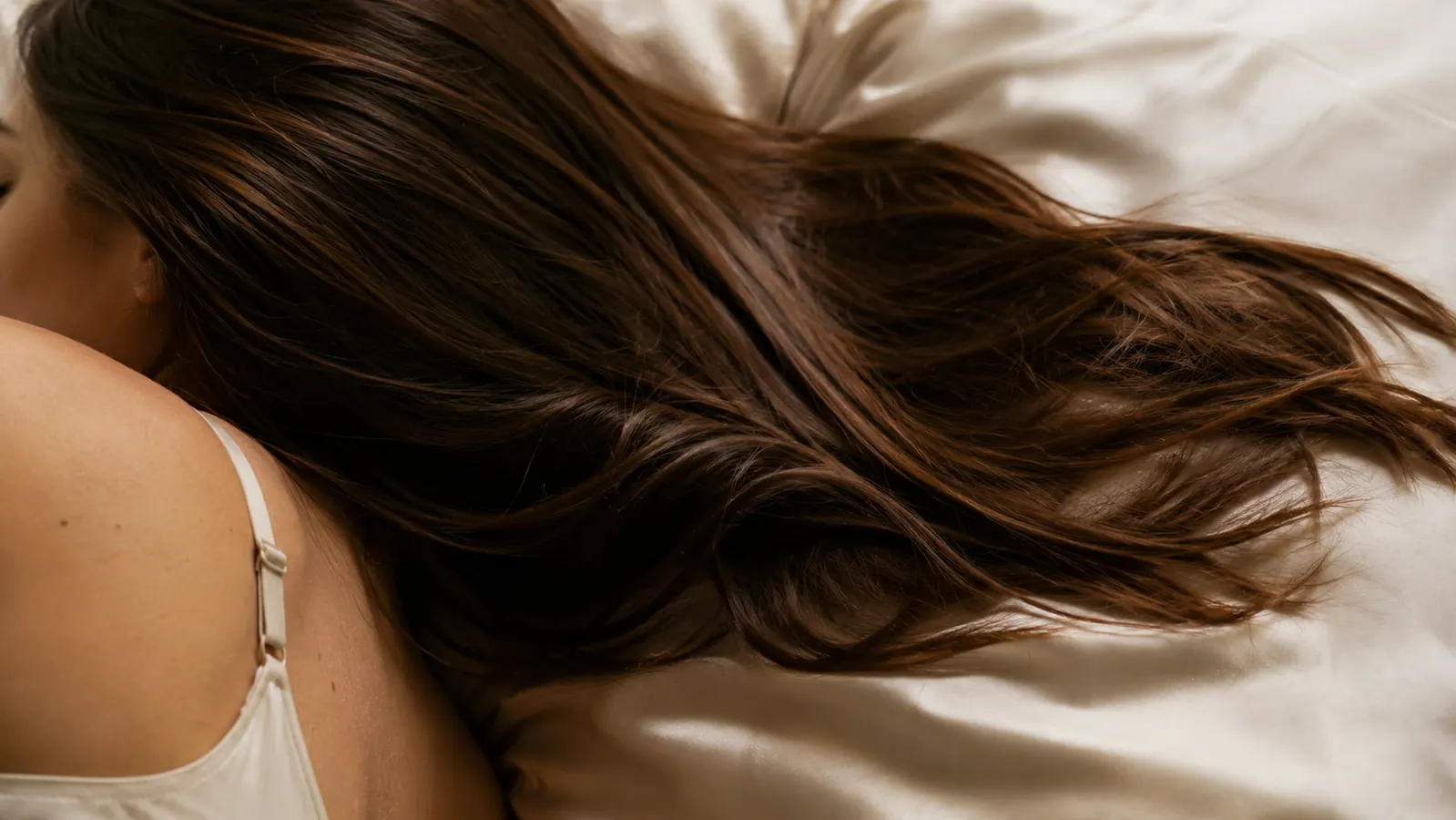 Close view of loose hair resting smoothly across a silk pillowcase in morning light, no visible tangling